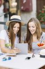 Zwei junge Freundinnen schauen auf digitales Tablet im Bürgersteig-Café — Stockfoto