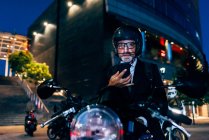 Homem de negócios maduro sentado em moto com smartphone — Fotografia de Stock