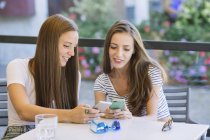 Дві молоді друзі-жінки дивляться на смартфони в тротуарному кафе — стокове фото