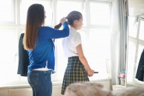 Mother putting teenage schoolgirl daughter's hair in ponytail — Stock Photo