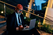 Reifer Geschäftsmann sitzt mit Laptop und Smartphone auf Stufen — Stockfoto