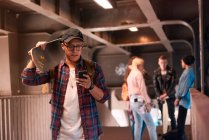Junger männlicher Skateboarder schaut auf städtischer Fußgängerbrücke aufs Smartphone — Stockfoto
