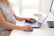 Cortado tiro de la mujer embarazada escribiendo en el ordenador portátil - foto de stock