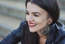 Retrato de mujer joven sonriendo, tatuajes en el cuello, nariz y piercings de oreja, primer plano - foto de stock