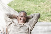 Man in hammock, hands behind head looking at camera smiling — Stock Photo