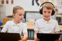 Écolier écoutant des écouteurs en classe à l'école primaire, portrait — Photo de stock