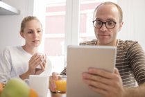 Mujer joven y novio mirando en la tableta digital en la mesa de desayuno - foto de stock