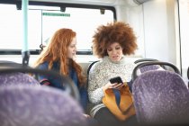 Две молодые женщины в автобусе смотрят на смартфон — стоковое фото