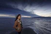 Junge Frau blickt am windigen Strand auf Staub — Stockfoto