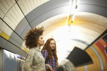 Dos mujeres jóvenes en la plataforma del metro esperando el tren - foto de stock