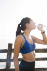 Jovem mulher bebendo água engarrafada durante o treinamento — Fotografia de Stock