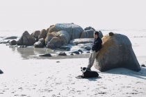 Homme adulte moyen avec chien appuyé contre un rocher regardant la mer, Cape Town, Western Cape, Afrique du Sud — Photo de stock