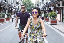 Casal de hipster étnico multi ciclismo ao longo da rua da cidade, Shanghai French Concession, Shanghai, China — Fotografia de Stock