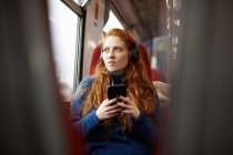 Mujer en tren escuchando música con teléfono móvil - foto de stock