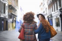 Dos mujeres jóvenes caminando brazo en brazo en la calle - foto de stock
