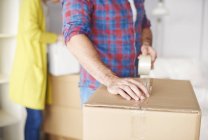 Young couple moving home, young man taping up cardboard box, mid section — Stock Photo
