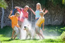 Family spraying dog with water from hosepipe — Stock Photo
