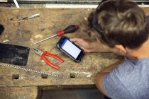 Overhead view of man in workshop using smartphone — Stock Photo