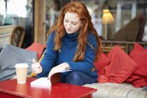 Woman at coffee shop writing in notepad — Stock Photo
