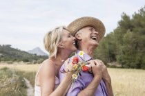 Paar auf dem Feld mit Blumenstrauß umarmt und lächelt — Stockfoto