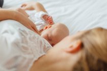 Young woman lying on bed with baby daughter — Stock Photo