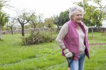 Старша жінка в саду, спираючись на садовий інструмент — стокове фото