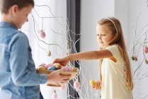 Девочка и брат украшают ветки яркими пасхальными яйцами — стоковое фото