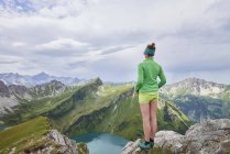 Vista trasera del excursionista femenino en el borde rocoso mirando las montañas de Tannheim, Tirol, Austria - foto de stock