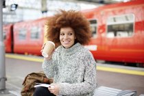 Donna con libro e tazza usa e getta sulla piattaforma della stazione ferroviaria — Foto stock