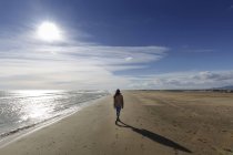 Rückansicht einer jungen Frau, die am Strand spazieren geht — Stockfoto