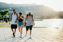 Tres jóvenes amigos paseando por el paseo marítimo, Lago de Como, Lombardía, Italia - foto de stock
