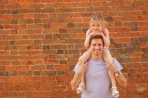 Portrait of mid adult man carrying daughter on shoulders by brick wall — Stock Photo