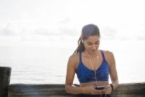 Молодая женщина тренируется на берегу моря и с помощью смартфона — стоковое фото