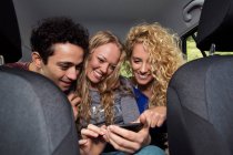 Amigos no banco de trás do carro olhando para o smartphone — Fotografia de Stock