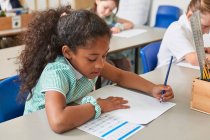 Школярка, що пише за столом у класі на уроці початкової школи — стокове фото