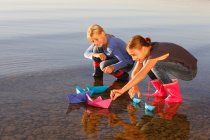Дві молоді дівчата плавають паперовими човнами на воді — стокове фото