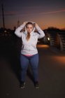 Portrait of curvaceous young woman getting hoody on footbridge at night — Stock Photo