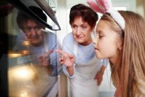 Girl and grandmother watching easter biscuits in kitchen oven — Stock Photo