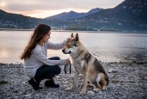 Молодая женщина ласкает собаку на берегу реки, Веркураго, Ломбардия, Италия — стоковое фото