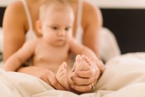 Woman holding baby daughters bare feet on bed — Stock Photo