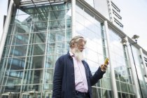 Reifer Mann fährt mit Smartphone gegen Bürogebäude — Stockfoto