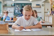 Écolière écrivant en classe leçon à l'école primaire — Photo de stock
