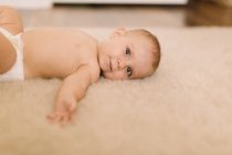 Retrato de bebê bonito menina na fralda deitada no tapete bege — Fotografia de Stock
