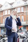 Älterer Mann steht neben Fahrrad und spricht mit Smartphone — Stockfoto
