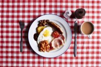 Full English breakfast on checked table cloth, overhead view — Stock Photo