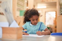 Écolière écrivant au bureau de classe à l'école primaire — Photo de stock