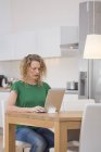 Жінка сидить за кухонним столом і використовує ноутбук — стокове фото