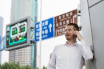 Joven hombre de negocios haciendo una llamada de teléfono inteligente en la ciudad, Shanghai, China - foto de stock