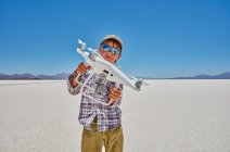 Retrato de niño en salinas, sosteniendo dron, Salar de Uyuni, Uyuni, Oruro, Bolivia, Sudamérica - foto de stock