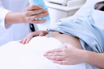 Vista recortada do ultrassonografista aplicando gel no estômago da paciente grávida — Fotografia de Stock